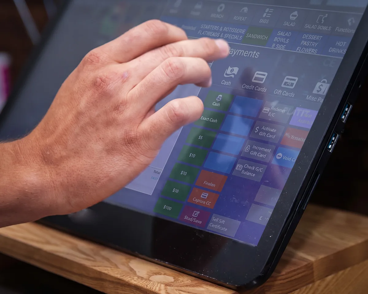 Restaurant POS touchscreen Hand tapping a payment screen on a touchscreen restaurant POS terminal
